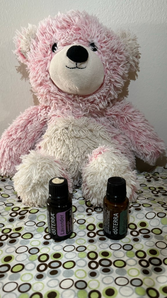 A pink teddy bear holds a bottle of Lavender essential oil in one paw and Balance in the other. 