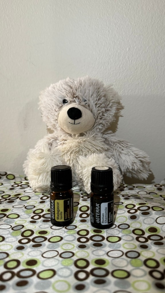 A small White teddy bear Warmie holds Roman Chamomile and Madagascar Vanilla essential oils from Doterra. 