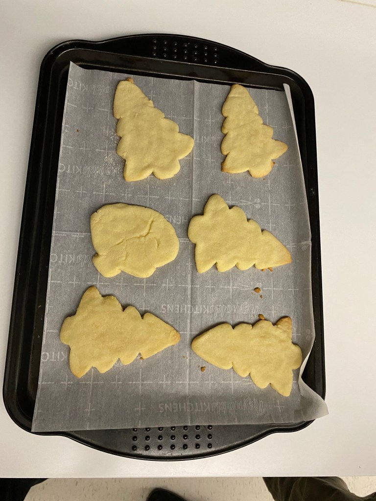 Six freshly baked Christmas tree shaped sugar cookies on a parchment paper-lined cookie sheet.