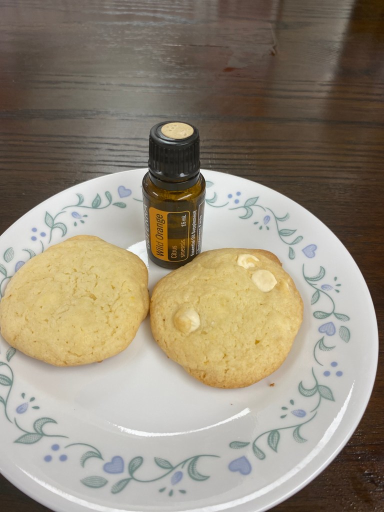 Two orange vanilla cake cookies on a plate with a bottle of Doterra Wild Orange essential oil between them.